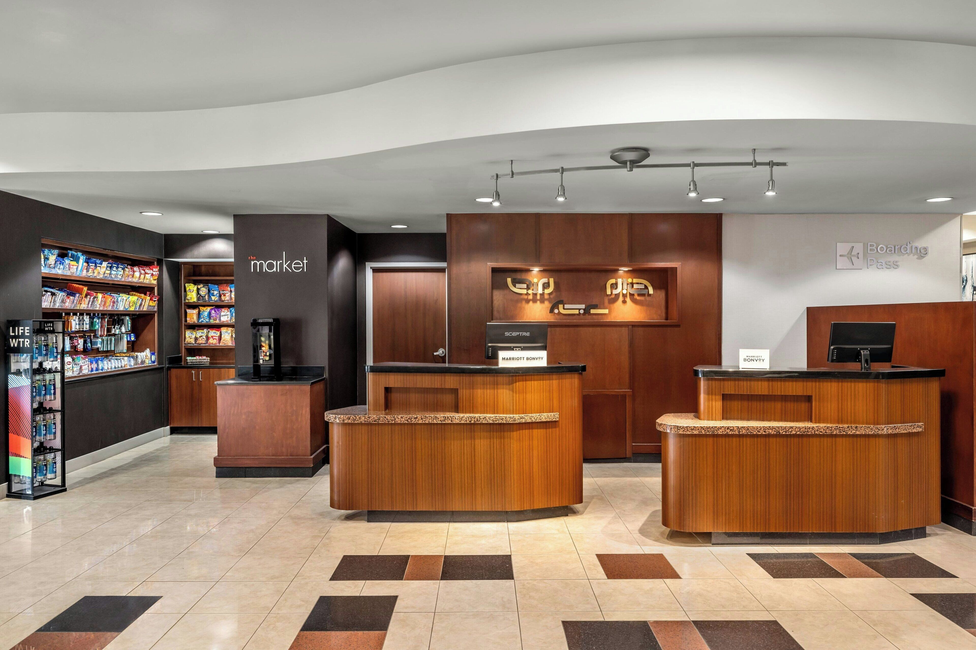 Un espace d’accueil d’hôtel avec un comptoir de réception en bois, une enseigne indiquant « marché » et une autre indiquant « carte d’embarquement ».