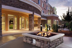 A hotel exterior with a stone fire feature, outdoor seating, and a curved building facade. - Courtyard Marriott Ankeny (Ankeny)