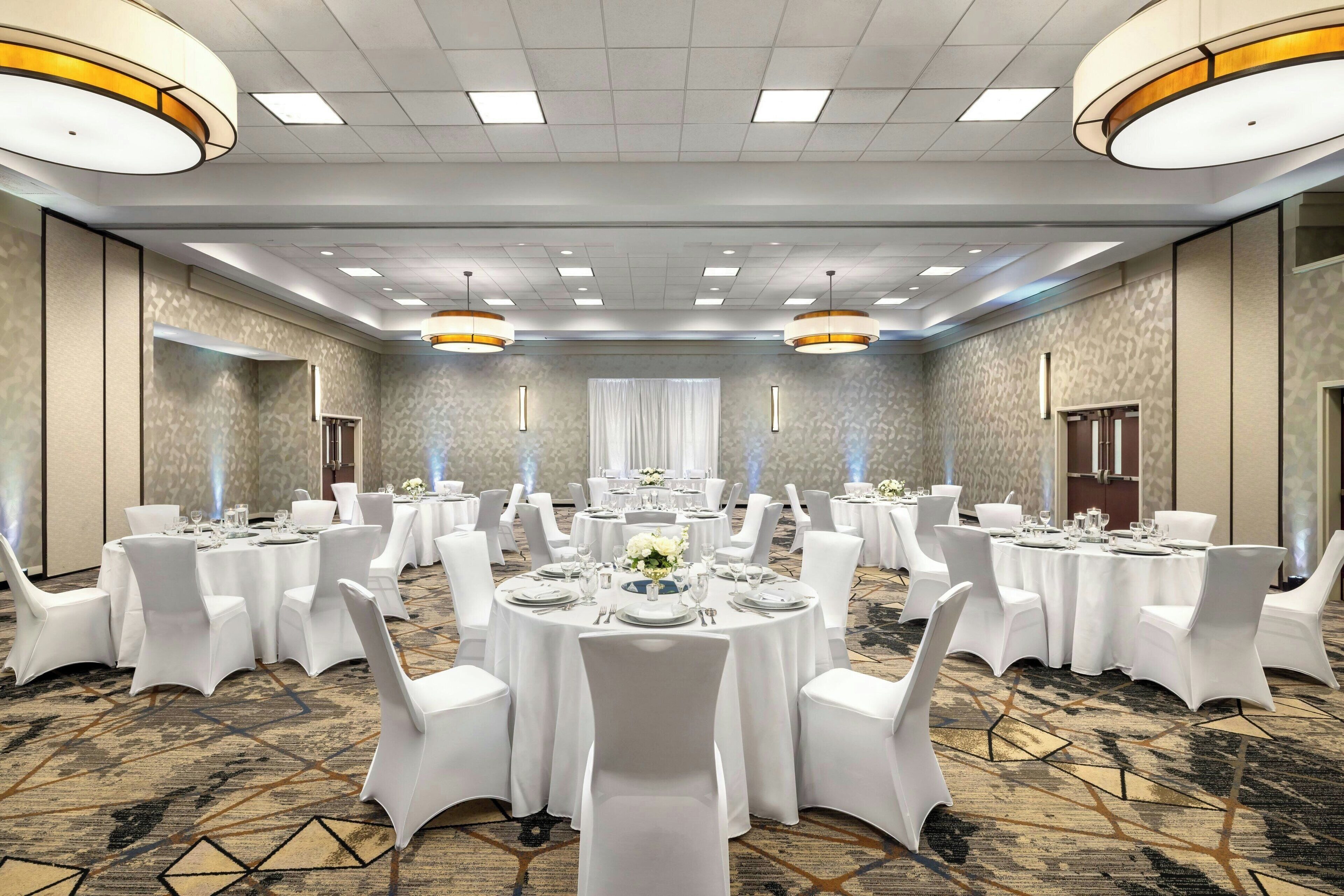 A large conference room with round tables, white chairs, and chandeliers.