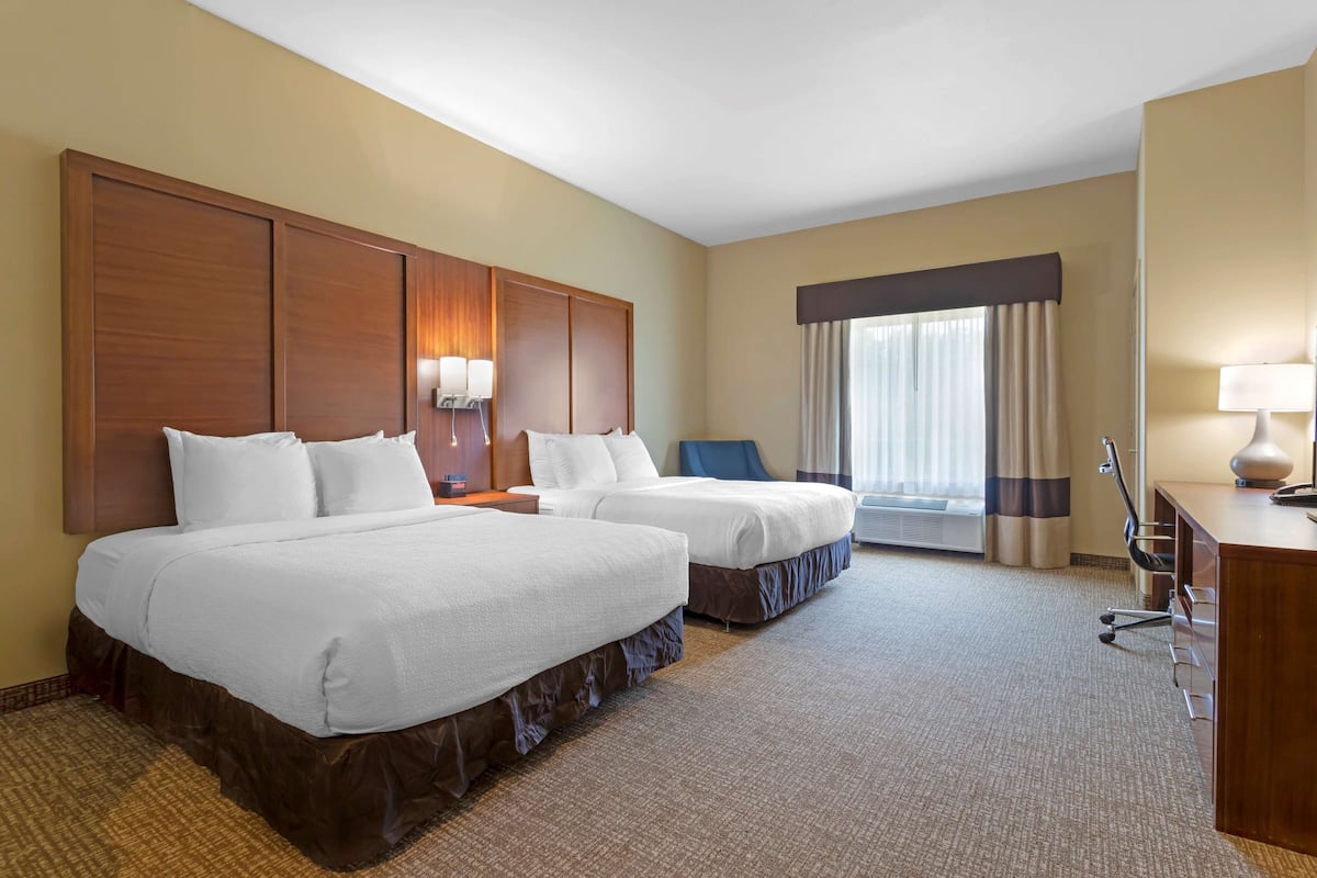 Habitación de hotel con dos camas, un escritorio, una silla y un ventanal con cortinas.