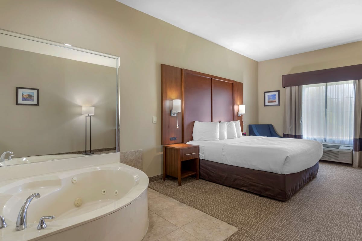 Habitación de hotel con una cama grande, baño separado con bañera y un amplio ventanal con cortinas.