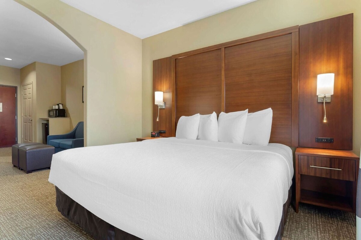 Habitación de hotel con una cama grande, dos mesitas de noche, un escritorio con una silla y un microondas en un estante.