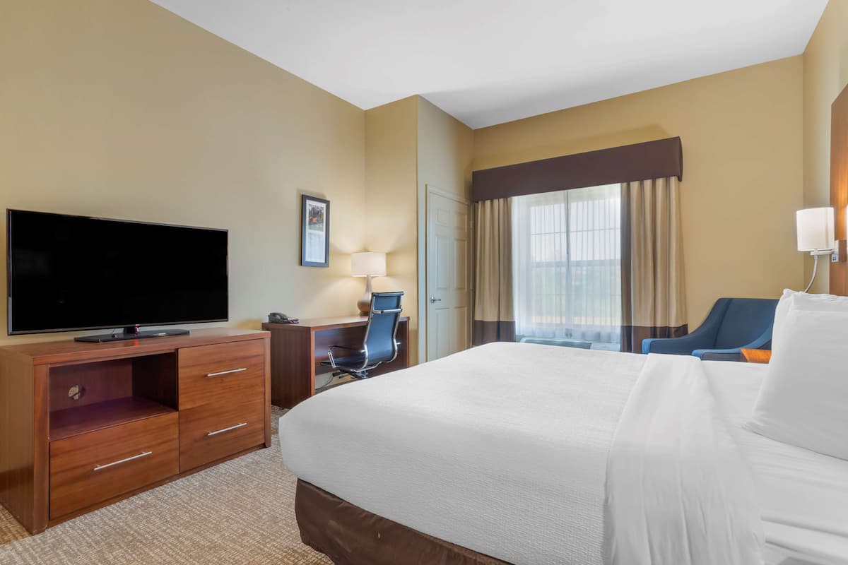 Habitación de hotel con una cama grande, un televisor de pantalla plana sobre una cómoda de madera, un escritorio con una silla y una ventana con cortinas.