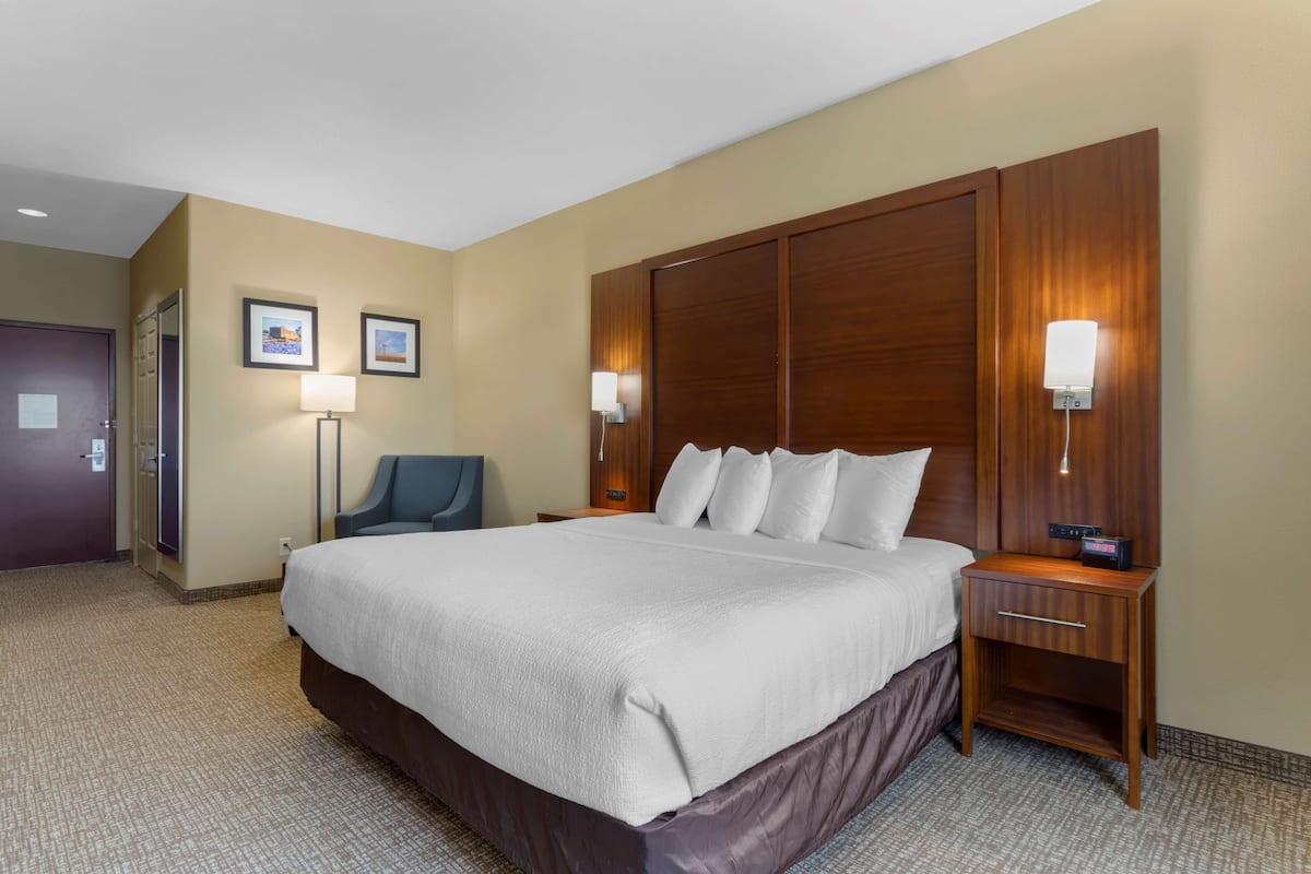 Habitación de hotel con una cama grande, cabecera de madera, dos lámparas de noche, un escritorio con un radio y una silla.