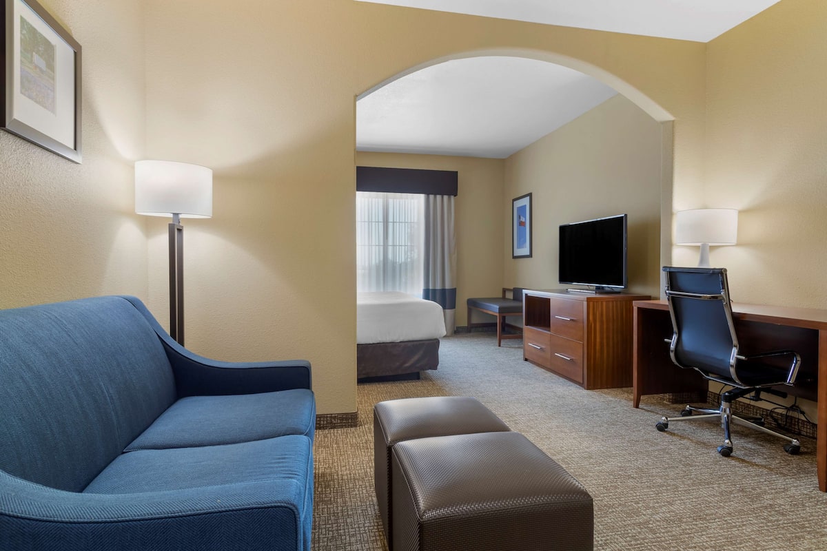Habitación de hotel con sofá azul, escritorio de madera, televisor y cama con ventana.