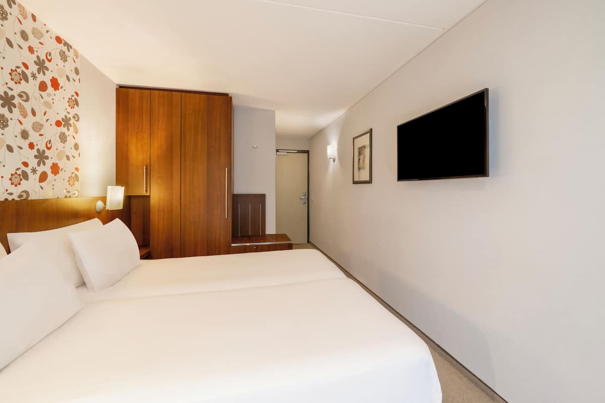 Habitación de hotel con una cama grande, armario de madera, televisor montado en la pared y puerta que da a un baño.