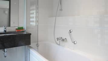 Un baño moderno con ducha envuelta en vidrio, bañera blanca y lavamanos con encimera negra.