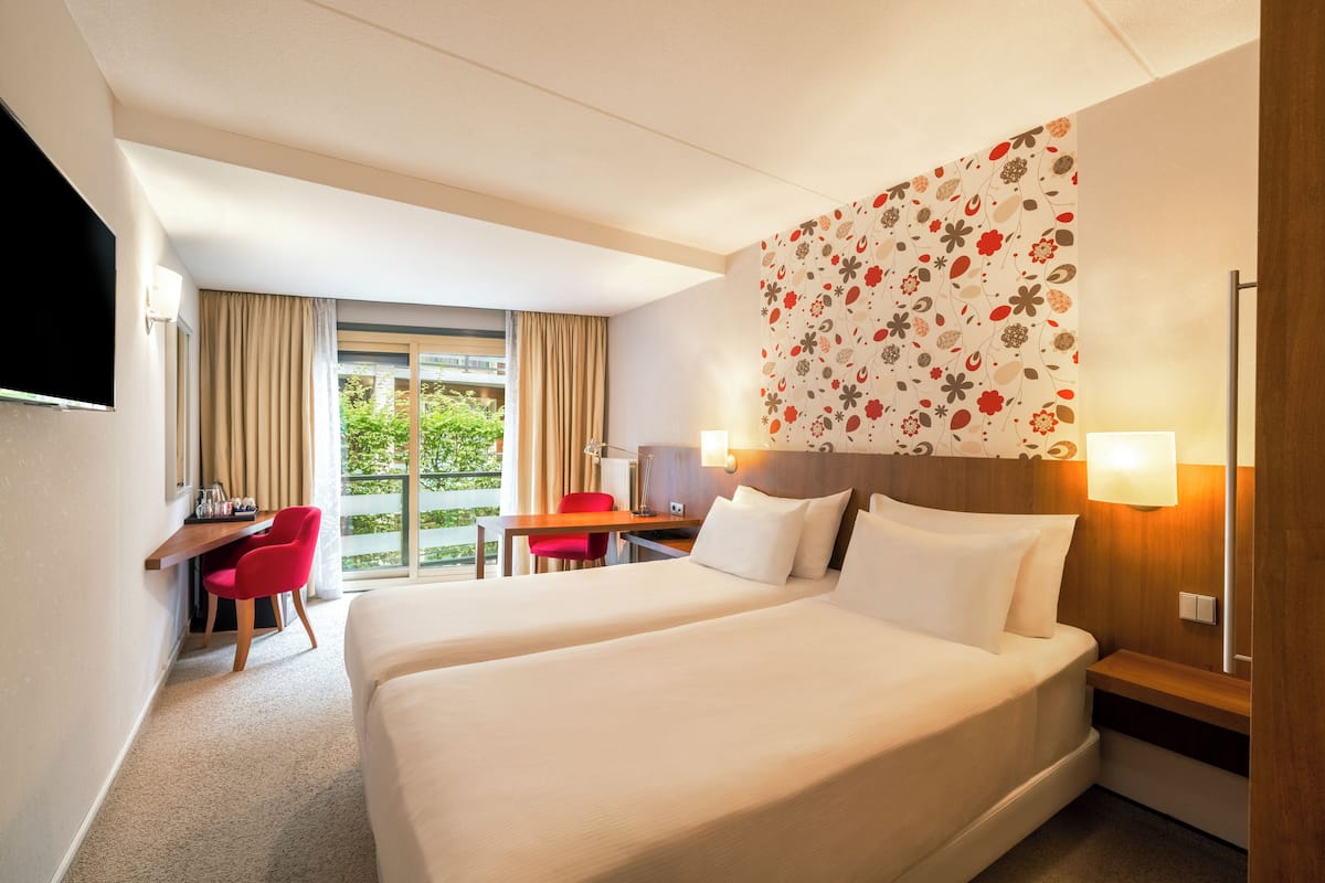 Habitación de hotel con dos camas, un escritorio, una silla, un televisor y una ventana con cortinas.