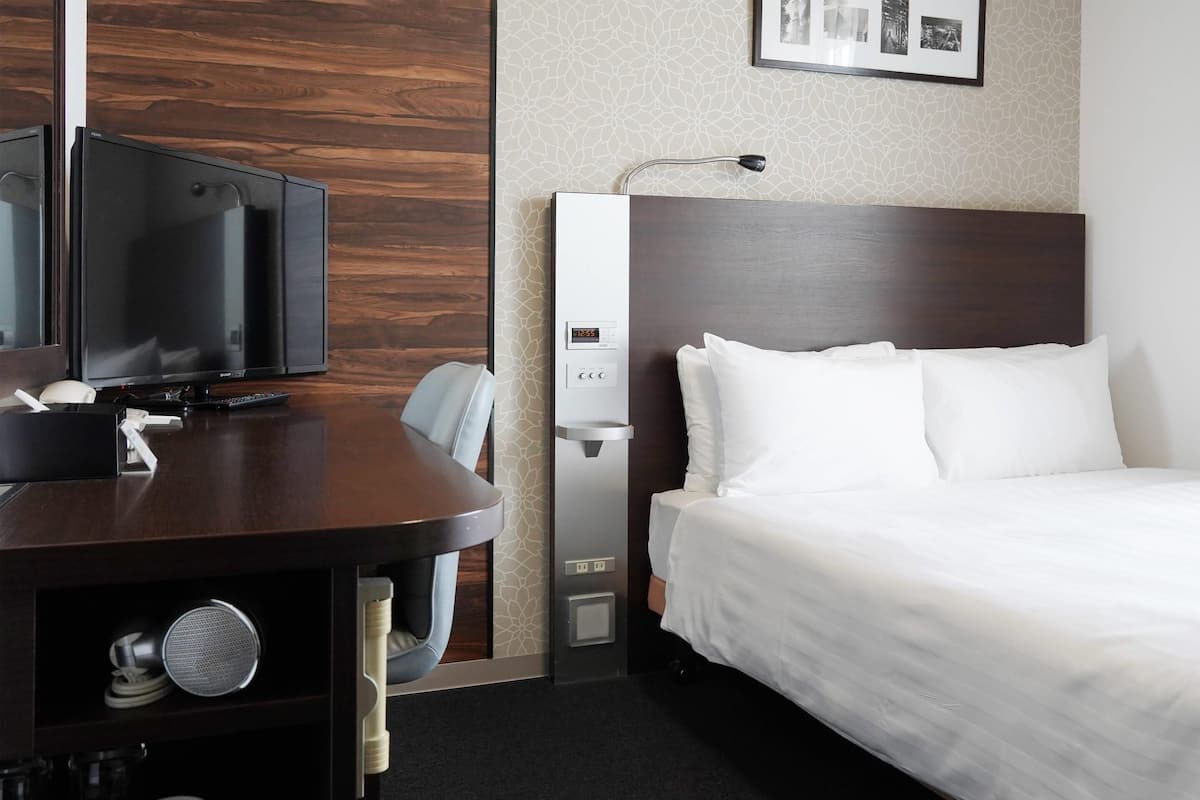 A hotel room with a bed, a desk with a television, a coffee machine, and a water dispenser.