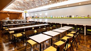 Un vaste espace dédié à la salle à manger, avec de longues tables et des chaises, un plancher en bois et un plafond orné de motifs.