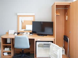 Habitación de hotel compacta con escritorio de madera, computadora, silla, espejo, refrigerador pequeño y zona de ducha.