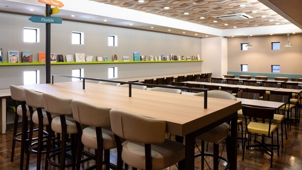 Une salle de conférence spacieuse, dotée de plusieurs tables et chaises, d’un plafond orné d’un motif géométrique et d’un mur décoré de tableaux encadrés.
