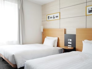 Hotellihuone, jossa on kaksi sänkyä, yöpöytä, seinään kiinnitetty valaisin ja sängyn yläpuolella oleva kehystetty taulu.