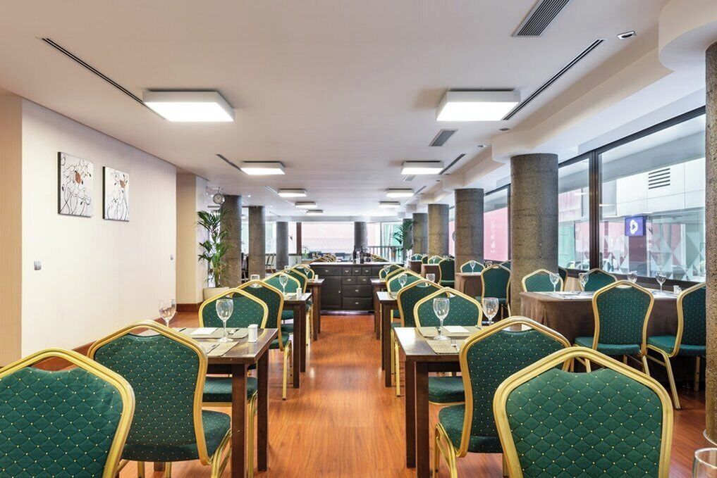 A restaurant with green upholstered chairs and tables, a wooden floor, and a view through large windows.