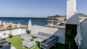 Eine Dachterrasse mit Blick auf das Meer, ein weißes Gebäude und eine Stadtlandschaft im Hintergrund.