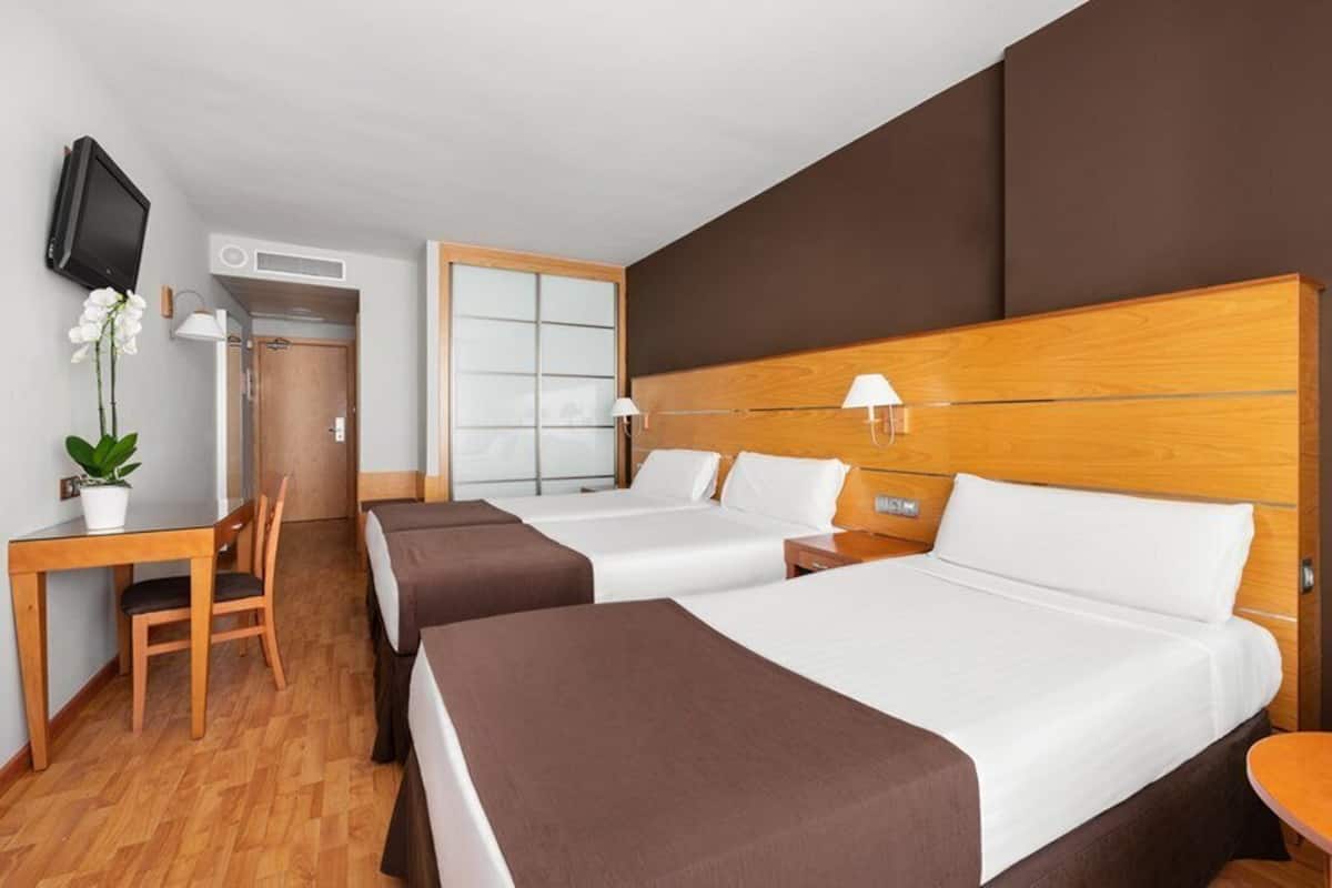 Ein Hotelzimmer mit zwei Betten, einem Schreibtisch, einem Stuhl, einem Fernseher und einem Fenster.
