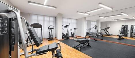Un gimnasio moderno con diversos equipos de ejercicio, suelo de madera y una amplia pared de espejos.