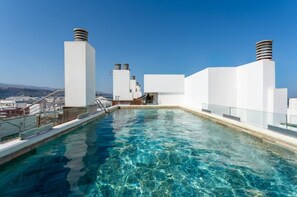 Una piscina en la azotea con agua azul cristalina, paredes blancas y varias chimeneas.