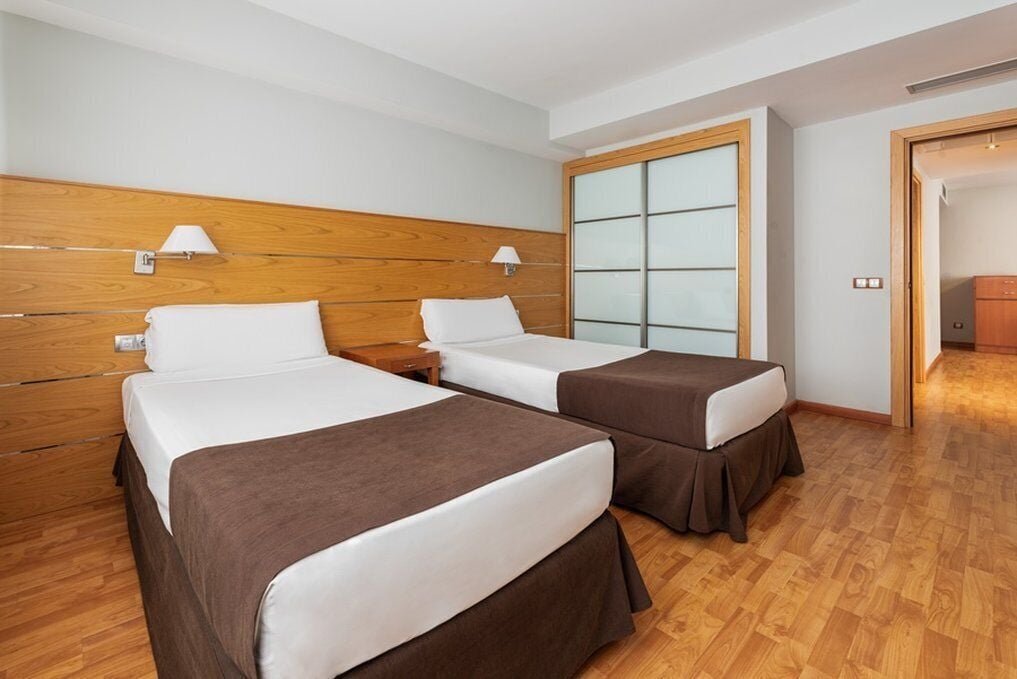 Una habitación de hotel con dos camas, cabeceros de madera, un ventanal grande y suelo de madera.