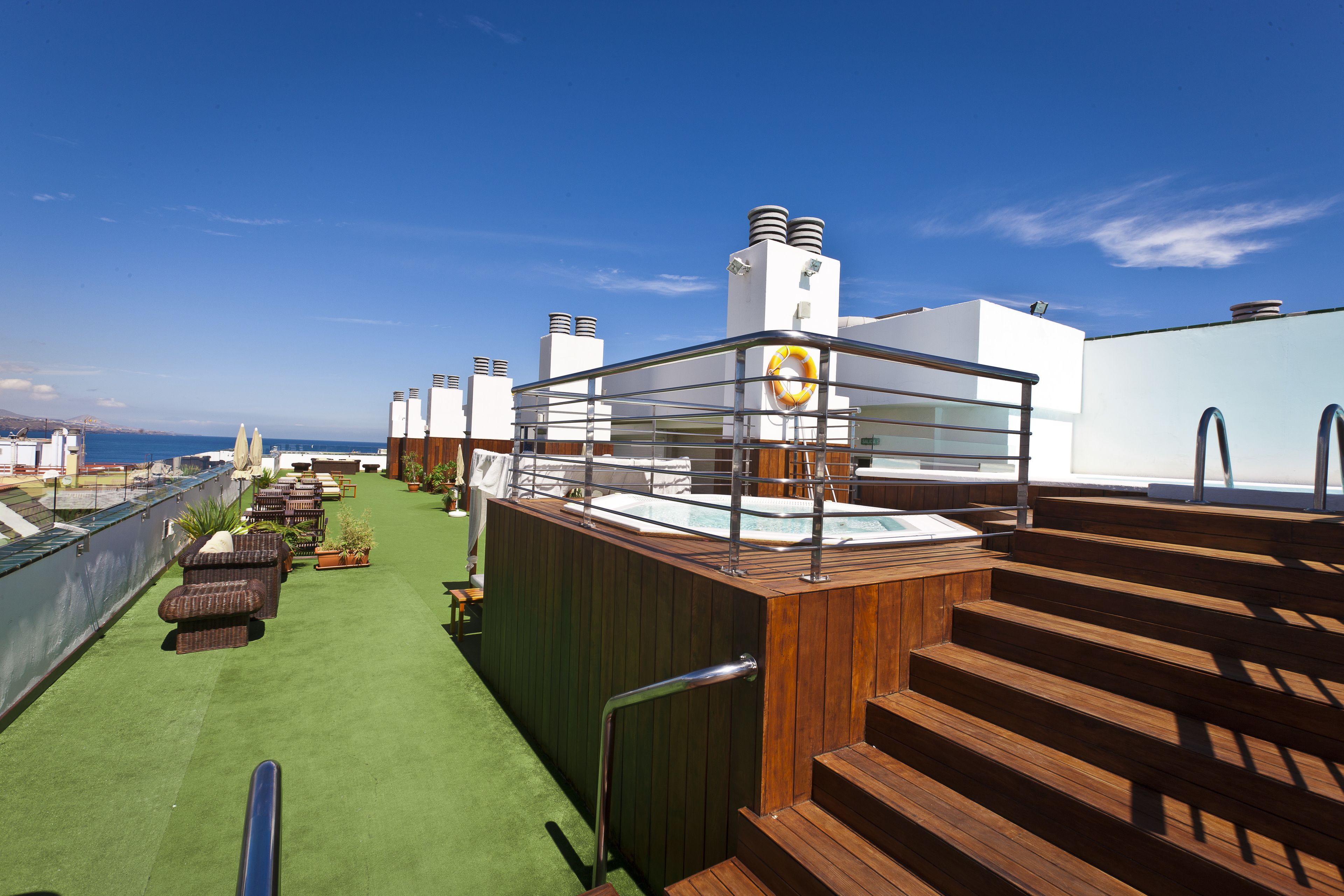 Een dakterras met een houten trap, een jacuzzi en buitenmeubels.