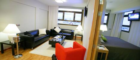 A modern living room with a black sofa, a red armchair, a coffee table, and a television on a stand.