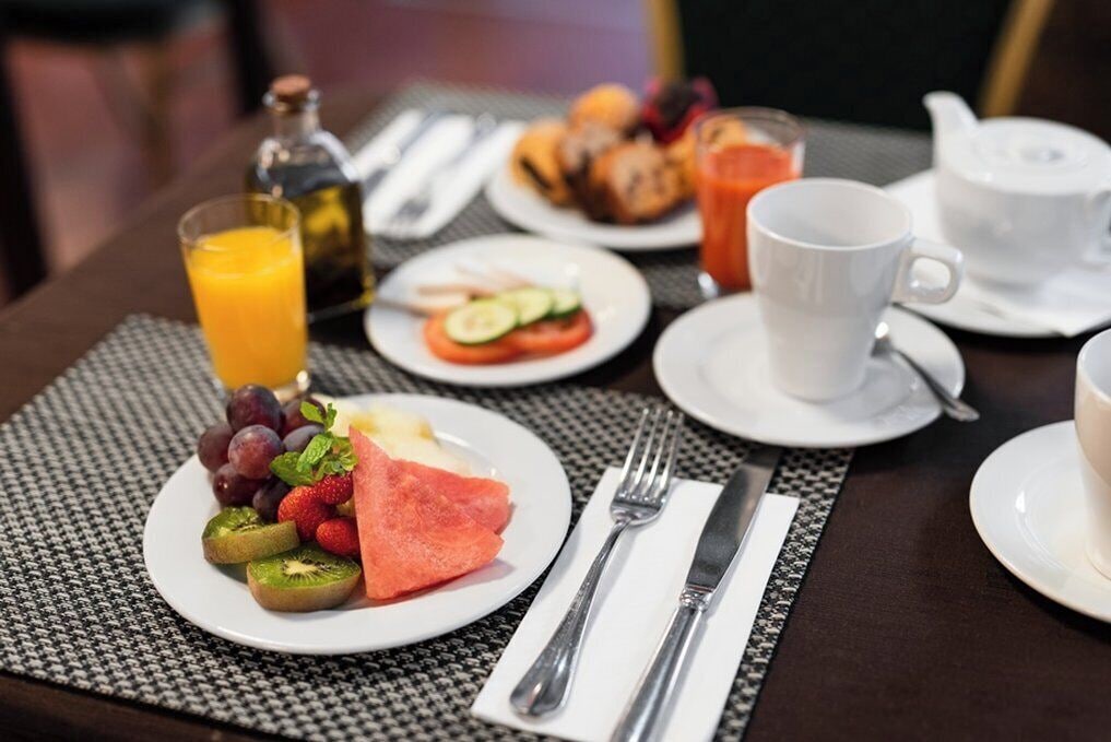 Un desayuno con platos de fruta, un vaso de jugo de naranja y una taza de café sobre una mesa.