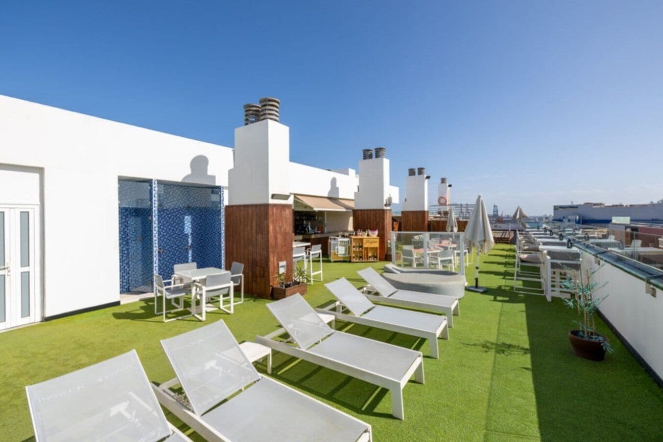 Terraço no telhado com cadeiras de lounge brancas, área de bar e vista da cidade.