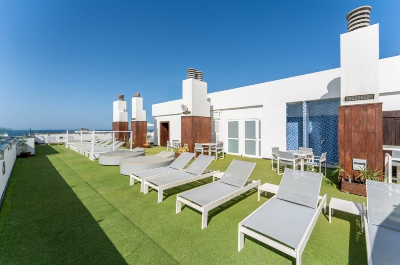 A rooftop terrace with white lounge chairs, a small pool, and a view of the sea.