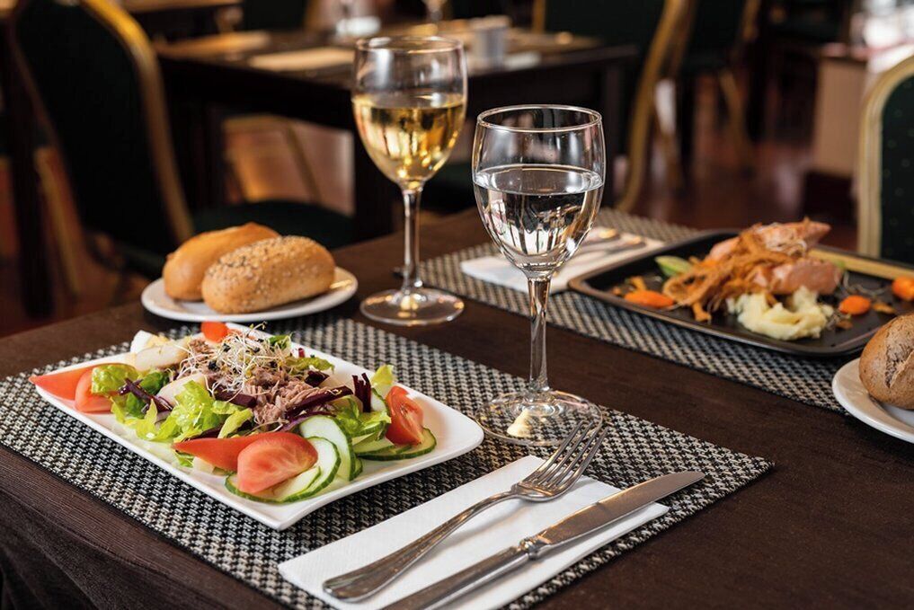 Une table à manger avec une salade, du pain et une assiette de nourriture, ainsi que deux verres de vin blanc.