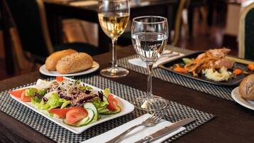 Une table à manger avec une salade, du pain et une assiette de nourriture, ainsi que deux verres de vin blanc.