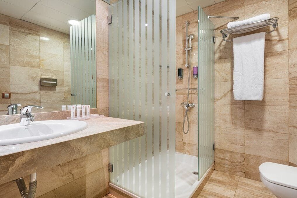 A modern bathroom with a glass-enclosed shower, a sink with a marble countertop, and a toilet.