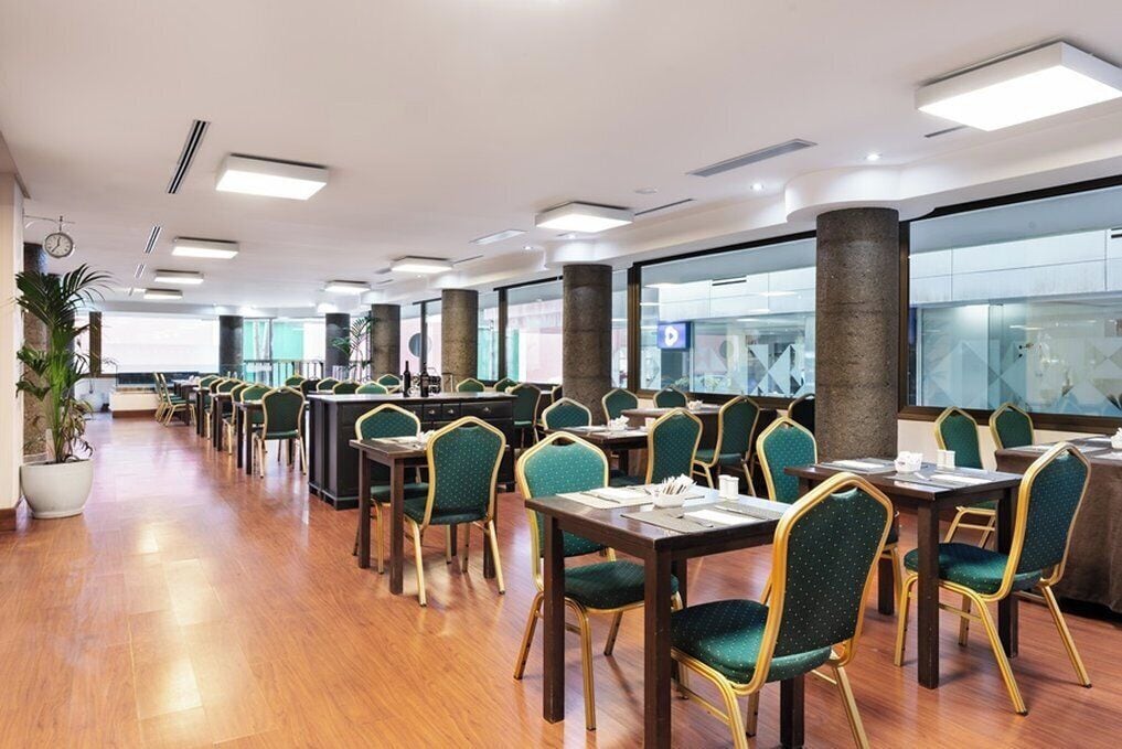 Un'ampia sala da pranzo con file di tavoli e sedie, ampie finestre e un pavimento in legno lucido.