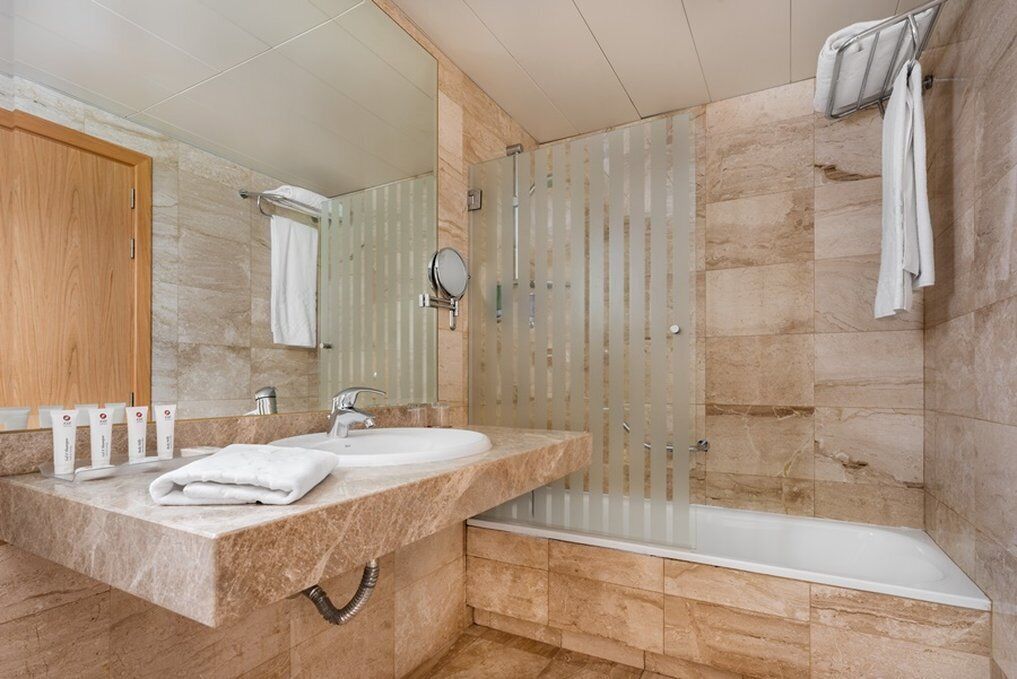 A modern bathroom with a marble countertop, two sinks, a large mirror, a glass shower enclosure, and a bathtub.