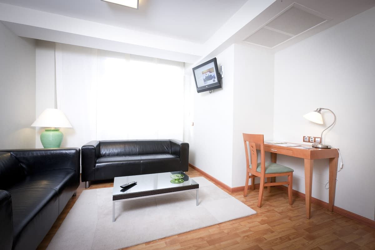 Ein modernes Wohnzimmer mit einem schwarzen Ledersofa, einem Glastisch, einem Holztisch mit Stuhl und einer Lampe.