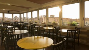 A spacious dining area with multiple round tables and chairs, large windows with a view of buildings and a dome structure. - Hotel Panorama (Florence)