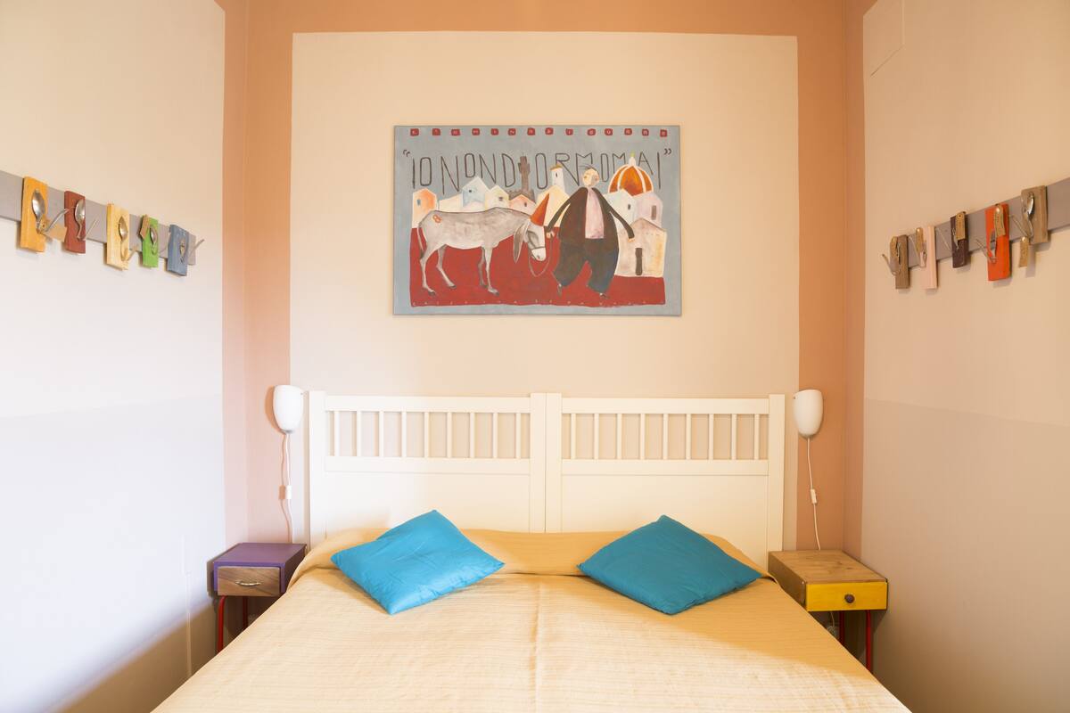 A bedroom with a bed, two pillows, a nightstand, a wall clock, and a painting.