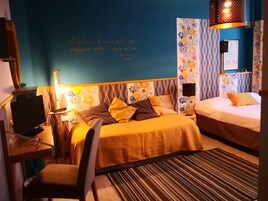 A hotel room with a bed, a desk, a chair, a TV, and a wall with a floral pattern.