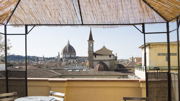 A terrace with tables and chairs, a thatched roof, and a view of a historic building with a dome and tower. - Hotel Panorama (Florence)