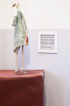 A sculpture on a red platform with a framed text on the wall behind it.