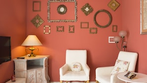 A room with a pink wall, two white armchairs, a small white table, a lamp, and various wall decorations. - Hotel Panorama (Florence)