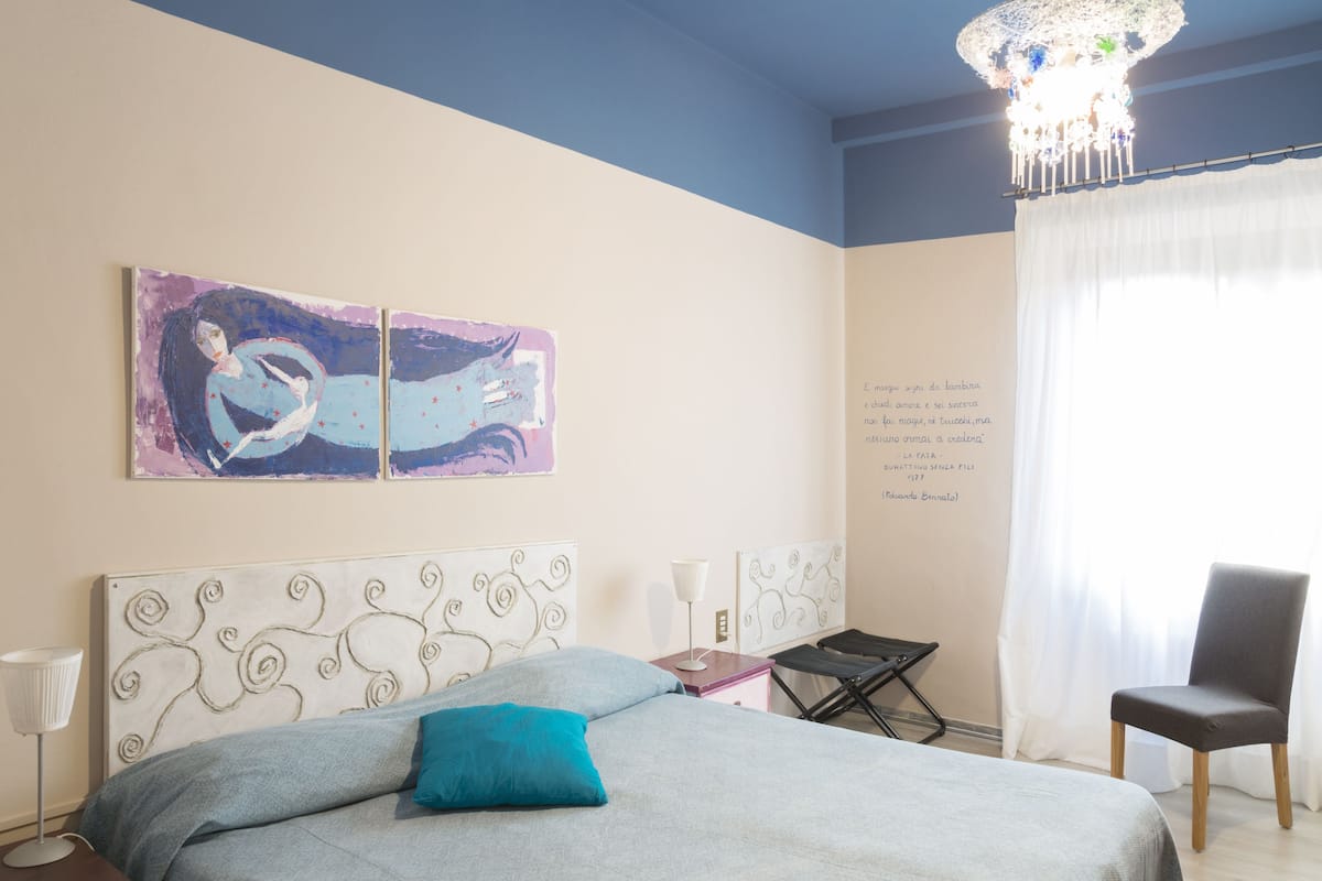 A bedroom with a bed, a chair, a table, and a chandelier.