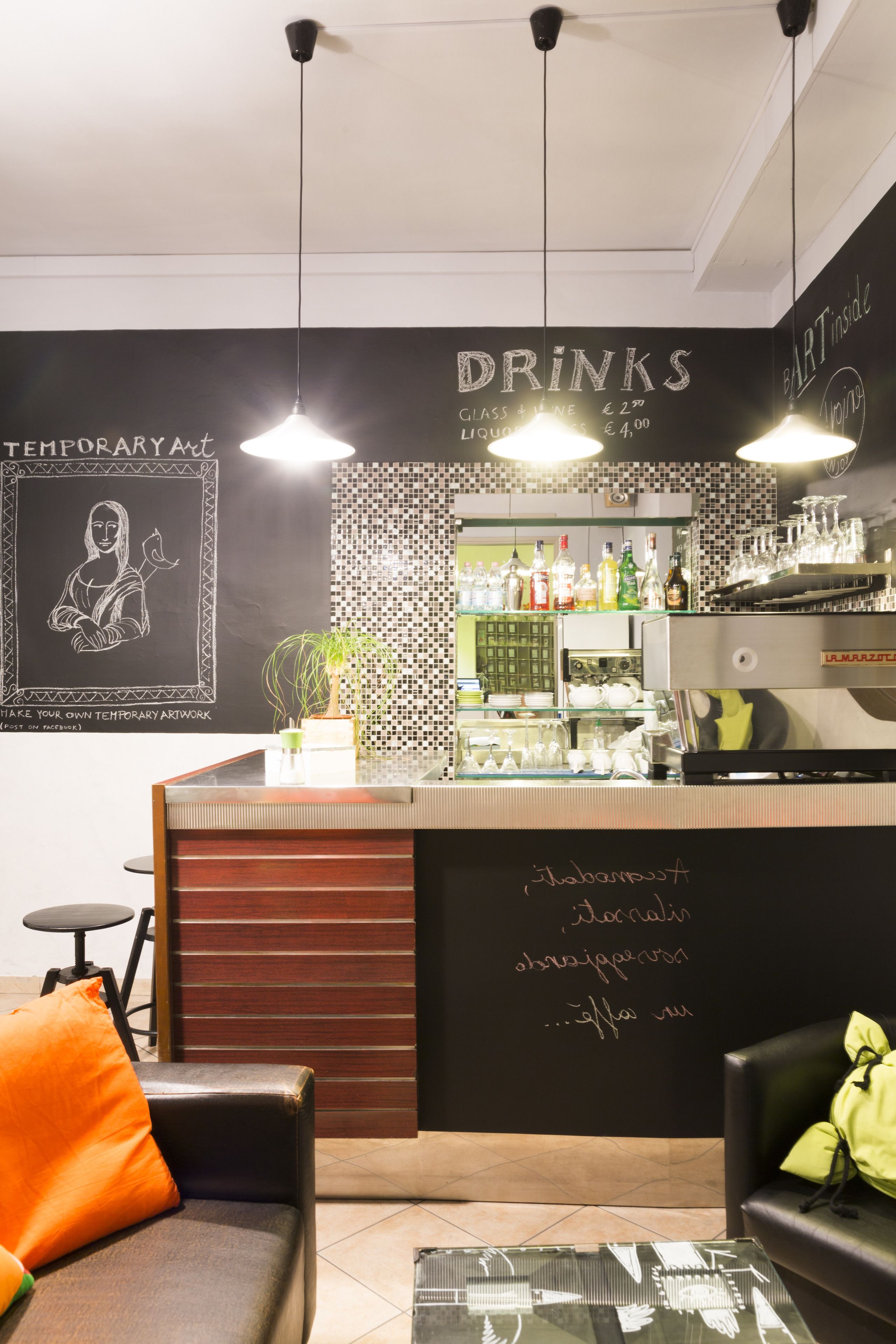 A bar area with a chalkboard menu, a coffee machine, and a seating area with a sofa and a table.