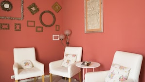 A room with two white armchairs, one with a floral pillow, a small round table with a book, and various wall decorations including framed pictures and a mirror. - Hotel Panorama (Florence)
