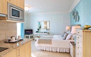 A hotel room with a kitchenette, a bed with a white bedspread, a bedside table with a lamp, a TV, and a mirror. - El Oceano Beach (Mijas)