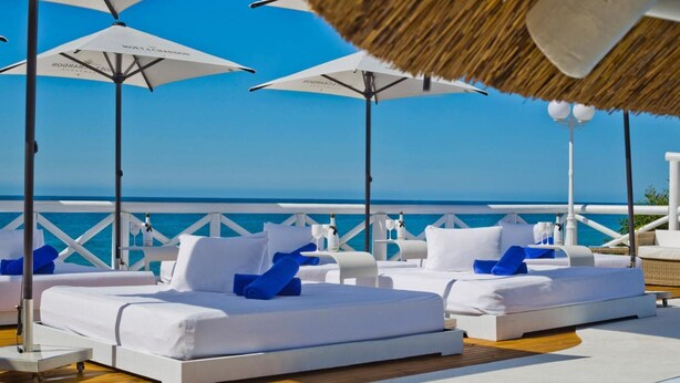 A beachside lounge area with white lounge chairs and umbrellas, a wooden deck, and a view of the ocean. - El Oceano Beach (Mijas)