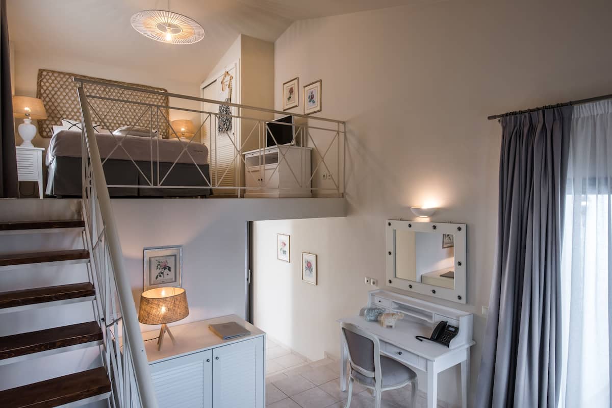 Un dormitorio con una cama, un escritorio con espejo, una lámpara y una escalera.