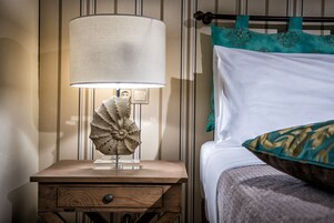 A wooden bedside table with a lamp and a decorative object, a bed with white bedding and teal pillows, and a striped wall.