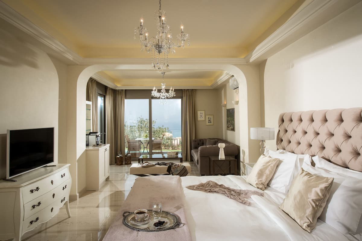Habitación de hotel con una cama grande, televisión, zona de comedor y vista al mar.