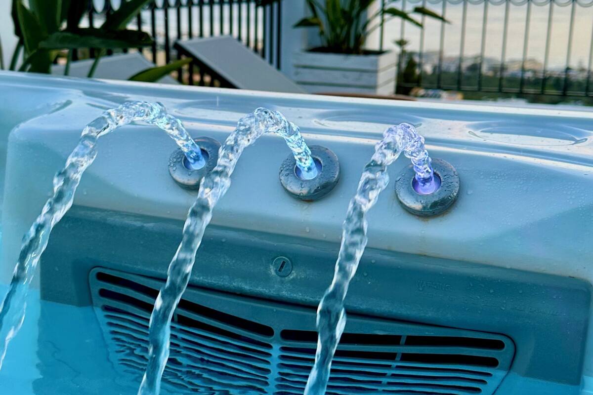 Un jacuzzi con tres chorros de agua, rodeado por una barandilla y macetas con plantas.