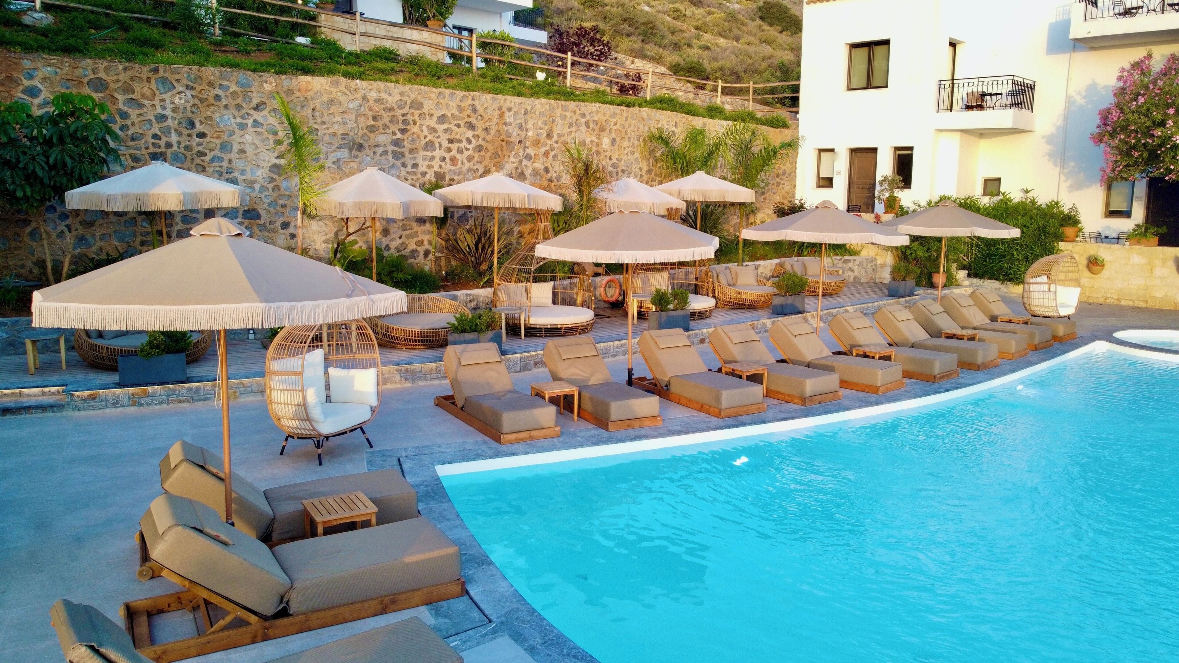 A poolside area with lounge chairs, umbrellas, and a stone wall.